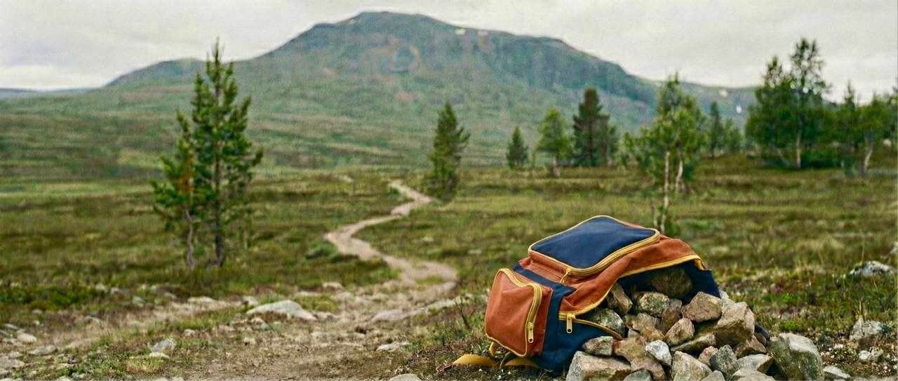 Una motxilla plena de pedres abandonada al peu d'un sender de muntanya — metàfora de l'esforç innecessari que carreguen els infants amb altes capacitats